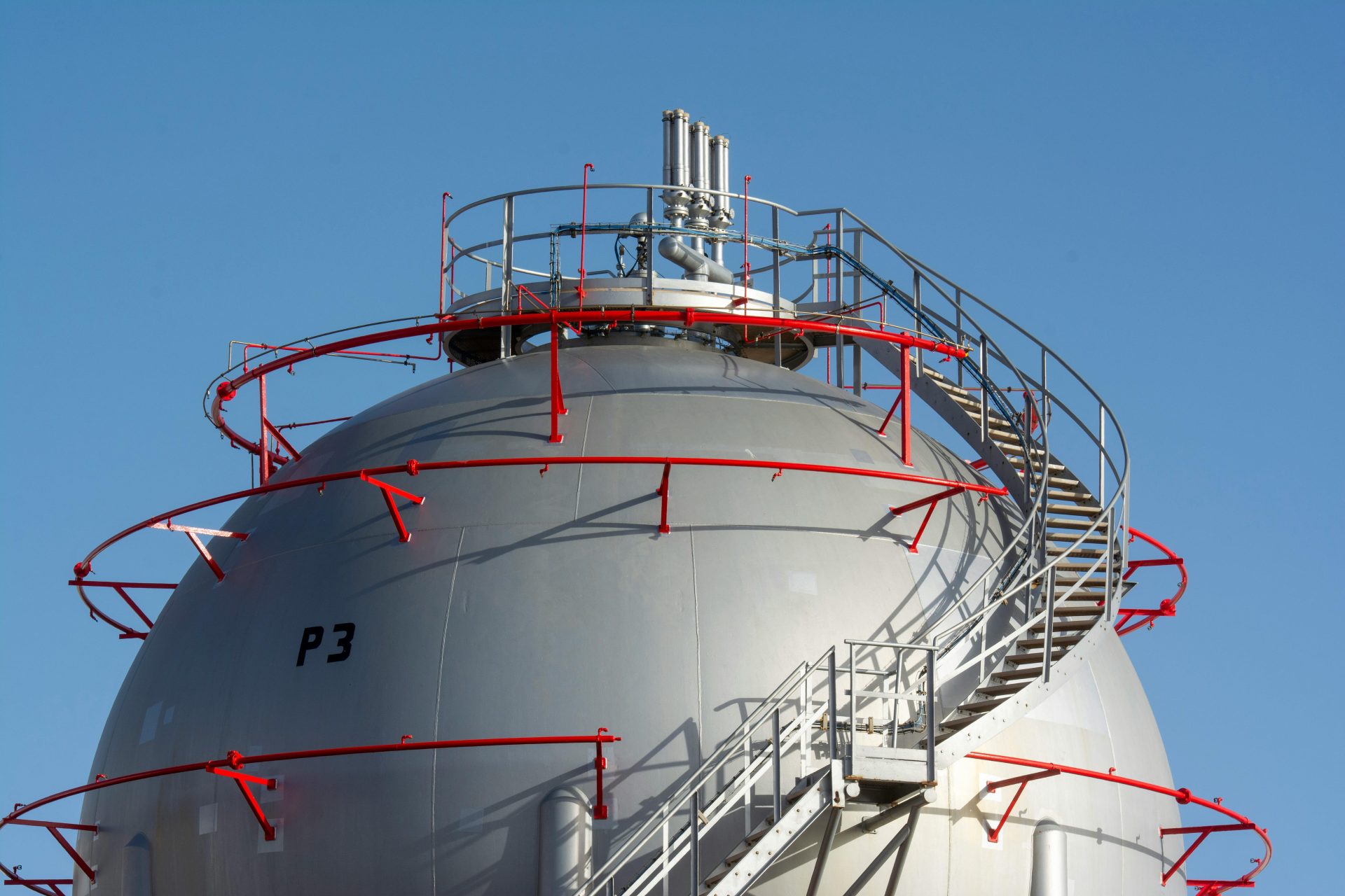 Close-up view of a large industrial gas storage sphere with a surrounding metal staircase.