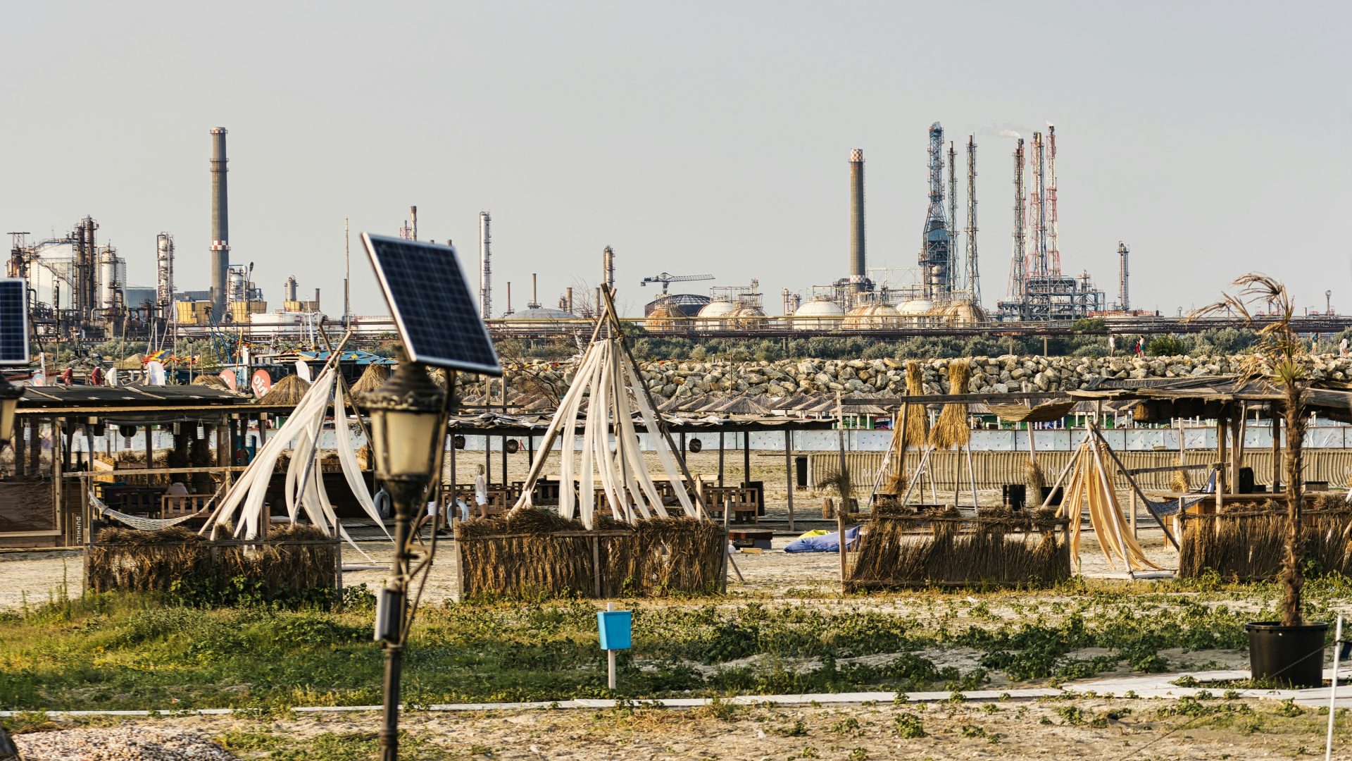 Beach huts are in front of an industrial landscape.